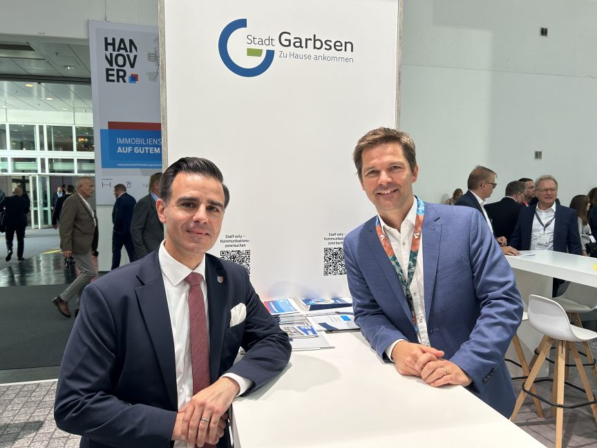 Zwei Männer in Anzügen sitzen an einem Messestand der Stadt Garbsen auf der Hannover Messe.