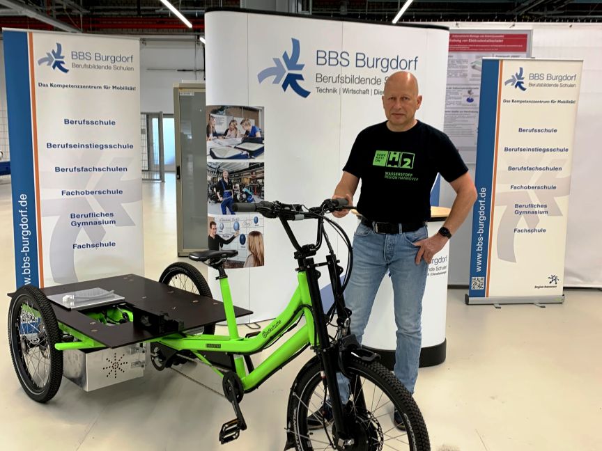 Mann steht neben grünem Elektro-Lastenrad vor BBS Burgdorf Berufsbildende Schulen Ausstellungsstand.