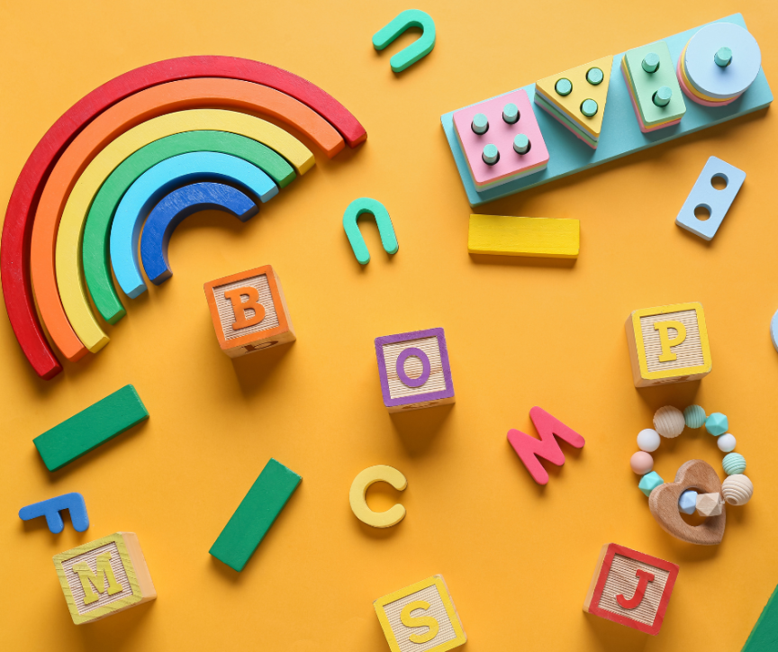 Bunte Holzspielzeuge auf orangem Hintergrund: Regenbogen, Buchstabenblöcke (B, O, P, M, C, S, J), Bausteine und Beißring.