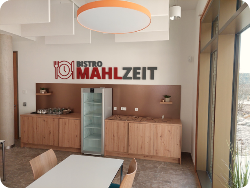Bistro Mahlzeit: Innenraum mit Holztheke, Kühlschrank, Tisch, Stühlen und Logo an der Wand.