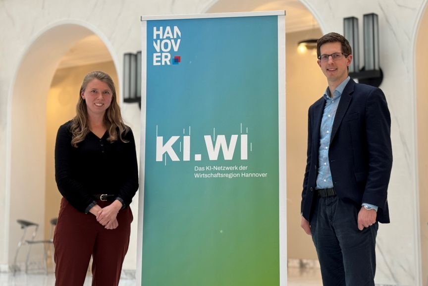 Zwei Personen stehen neben einem Banner mit der Aufschrift „KI.WI – Das KI-Netzwerk der Wirtschaftsregion Hannover".